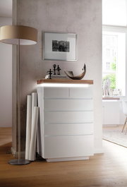 Moderne weiße Hochkommode mit fünf Schubladen, seitliche Perspektive, dekoriert mit Skulpturen und Büchern auf der Oberseite.