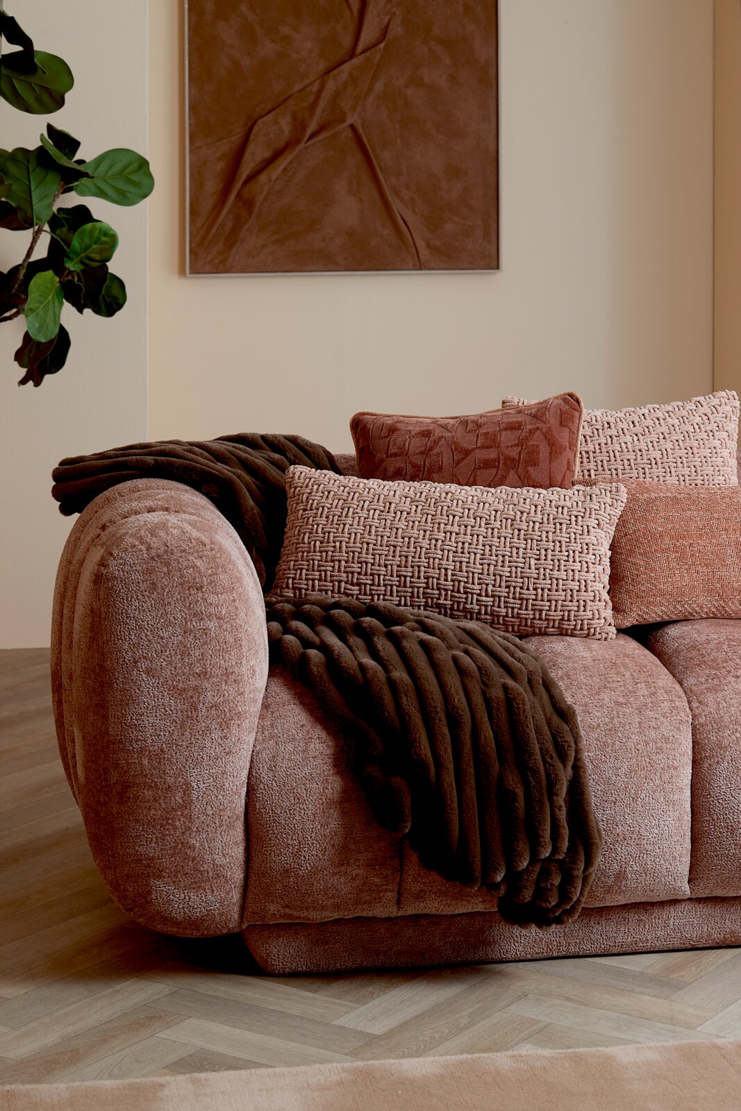 Light&Living Kissen HATO Frontale Nahaufnahme eines roséfarbenen Sofas mit abgerundeter Armlehne, strukturierten Zierkissen und dunkelbrauner Kuscheldecke in einem stilvollen Wohnzimmer.