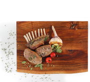 Vogelperspektive auf einen Hackblock aus Akazienholz mit gegrilltem Fleisch, Knoblauch und Tomaten als Dekoration.