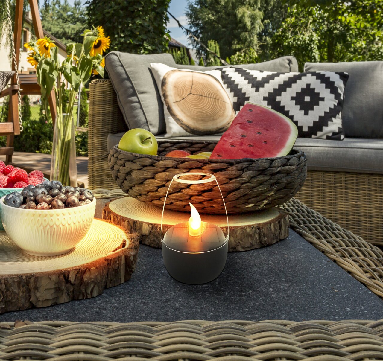 Solarleuchte in einem gemütlichen Gartenambiente, umgeben von Obst und dekorativen Kissen, aus der Perspektive eines niedrigen Tisches betrachtet.
