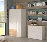 Modernes Wohnzimmer-Set mit weißem Kleiderschrank und passender Kommode mit Holzoptik-Akzenten, dekoriert mit Boxen, Büchern und Pflanzen; Perspektive: leicht schräg von vorn (Front-/Seitenansicht)