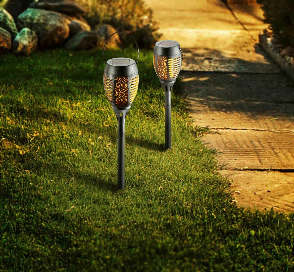 Ambia Garden Solarleuchte Flame II Zwei Solarleuchten Flame II mit flammenähnlichem Lichtmuster, auf einem Rasen neben einem Gehweg platziert, aus seitlicher Perspektive fotografiert.