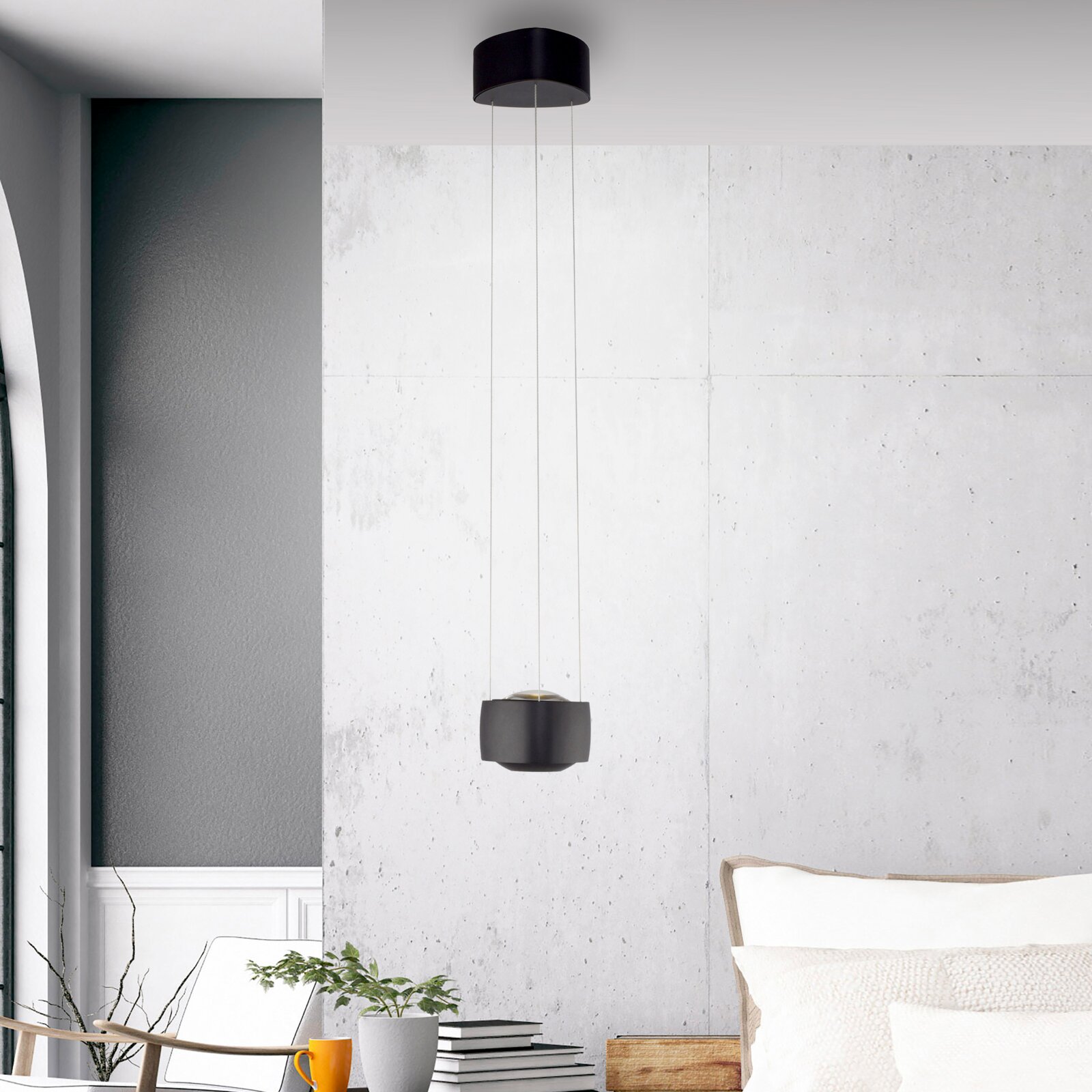 Moderne schwarze Pendelleuchte mit zylindrischer Deckenhalterung und kompaktem Lampenschirm an drei dünnen Seilen, frontal in leichter Untersicht vor heller Betonwand im Wohnraum