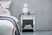Spiegelnde Nachtkommode mit Schublade und Ablage, darauf eine moderne Lampe und eine kleine Vase, seitliche Perspektive.