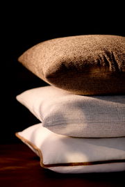 Drei übereinander gestapelte Kissen in verschiedenen Texturen und Farben, von der Seite betrachtet.