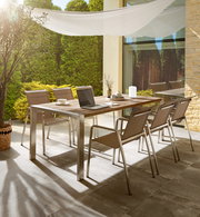 Moderner Gartentisch mit sechs Stühlen auf einer Terrasse, umgeben von grünen Pflanzen, aus seitlicher Perspektive fotografiert.