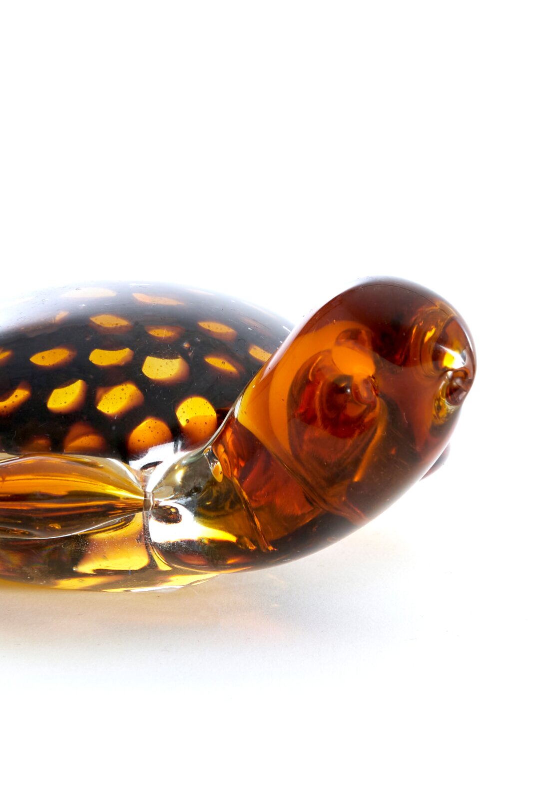 Nahaufnahme eines gläsernen Schildkrötenornaments mit bernsteinfarbenen und gelben Mustern, seitliche Perspektive.