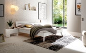Modernes Schlafzimmer mit einem weißen Holz- und Metallbett, seitlicher Blick. Das Bett ist mit grauer und olivgrüner Bettwäsche dekoriert, umgeben von stilvollen Accessoires und großen Fenstern, die viel Tageslicht hereinlassen.
