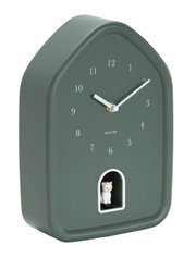 Moderne Wanduhr in Hausform mit grünem Gehäuse und weißem Zifferblatt, seitliche Perspektive, mit kleiner weißer Katzenfigur in einer Öffnung unten.