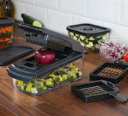 Zwiebel- und Gemüsehacker auf einer Küchenarbeitsplatte, gefüllt mit gewürfeltem Gemüse, mit einer roten Zwiebel auf der Schneidefläche. Perspektive von schräg oben.