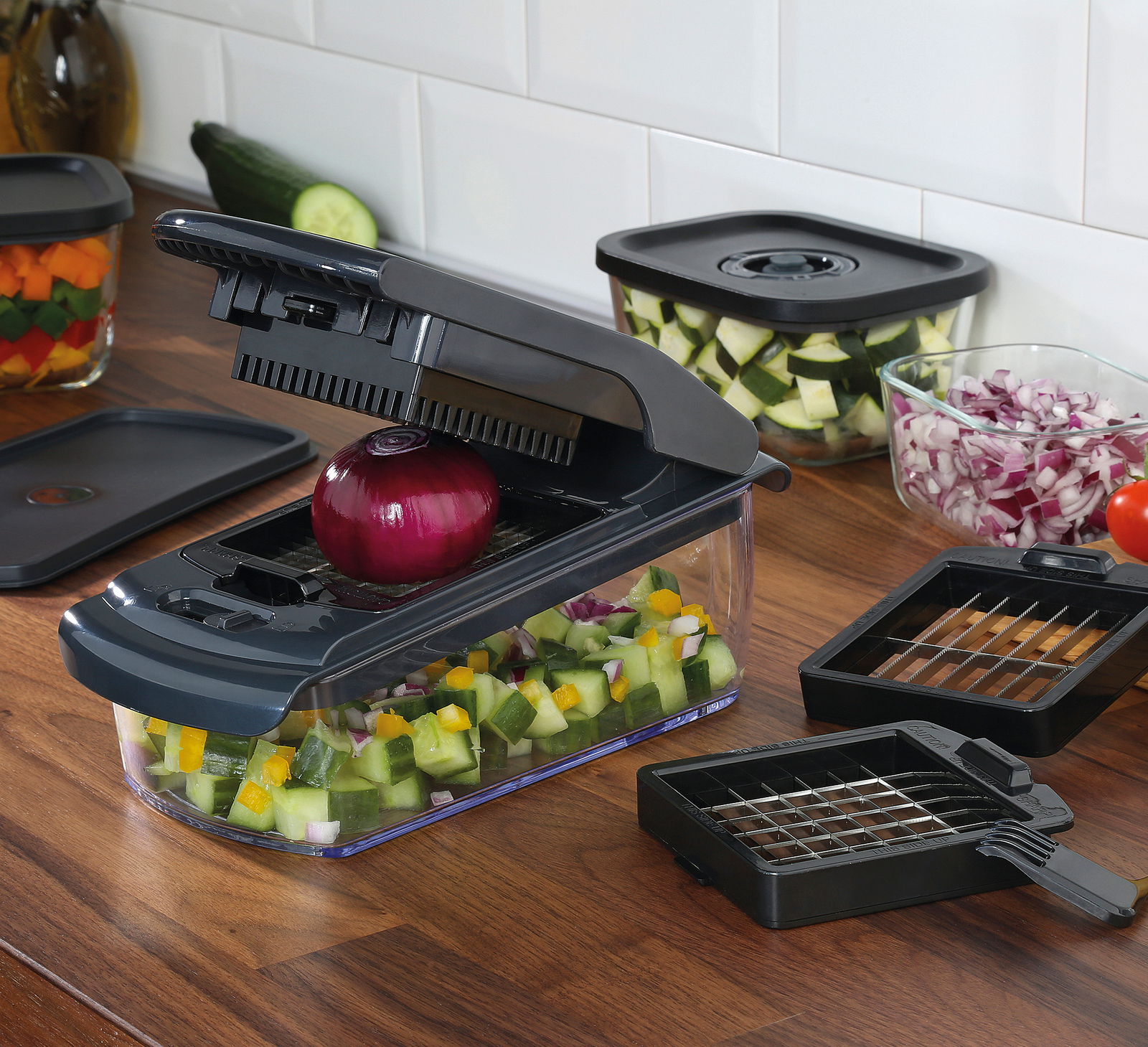 Zwiebel- und Gemüsehacker auf einer Küchenarbeitsplatte, gefüllt mit gewürfeltem Gemüse, mit einer roten Zwiebel auf der Schneidefläche. Perspektive von schräg oben.