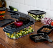 Zwiebel- und Gemüsehacker auf einer Küchenarbeitsplatte, gefüllt mit gewürfeltem Gemüse, mit einer roten Zwiebel auf der Schneidefläche. Perspektive von schräg oben.