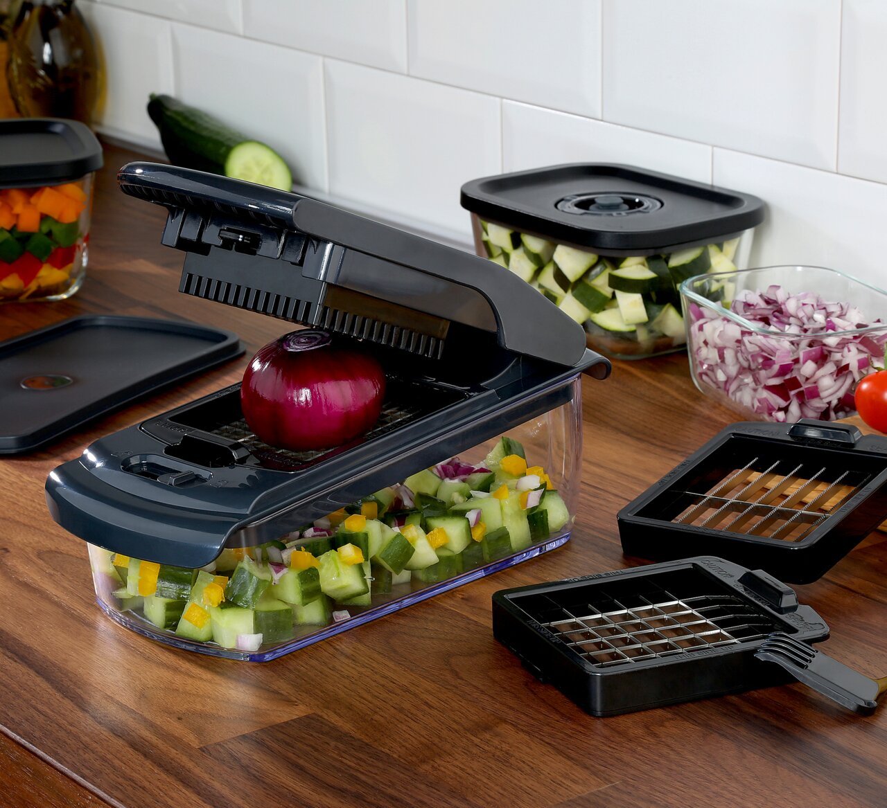 Zwiebel- und Gemüsehacker auf einer Küchenarbeitsplatte, gefüllt mit gewürfeltem Gemüse, mit einer roten Zwiebel auf der Schneidefläche. Perspektive von schräg oben.