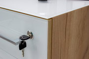 Nahaufnahme eines Aktenschranks mit Holzoptik und weißer Front, Schlüssel steckt im Schloss, seitliche Perspektive.