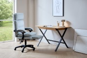 Moderner Schreibtisch mit Holzplatte und schwarzen Metallbeinen, seitliche Perspektive. Daneben ein ergonomischer Bürostuhl vor einem großen Fenster mit Blick ins Grüne.