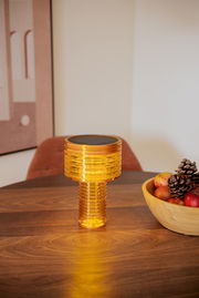 Akku-Solar-Tischleuchte in warmem Licht auf einem Holztisch, seitliche Perspektive