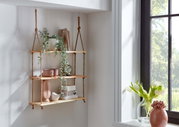 Wandhängeregal aus drei hellen Holzablagen an Juteseilen, dekoriert mit Pflanze und Accessoires, in heller Raumecke neben Fenster; Perspektive: frontale Ansicht leicht von rechts.