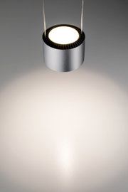 Moderne, zylindrische Pendelleuchte in Silber, von oben fotografiert, mit warmem Lichtstrahl auf einer grauen Oberfläche.