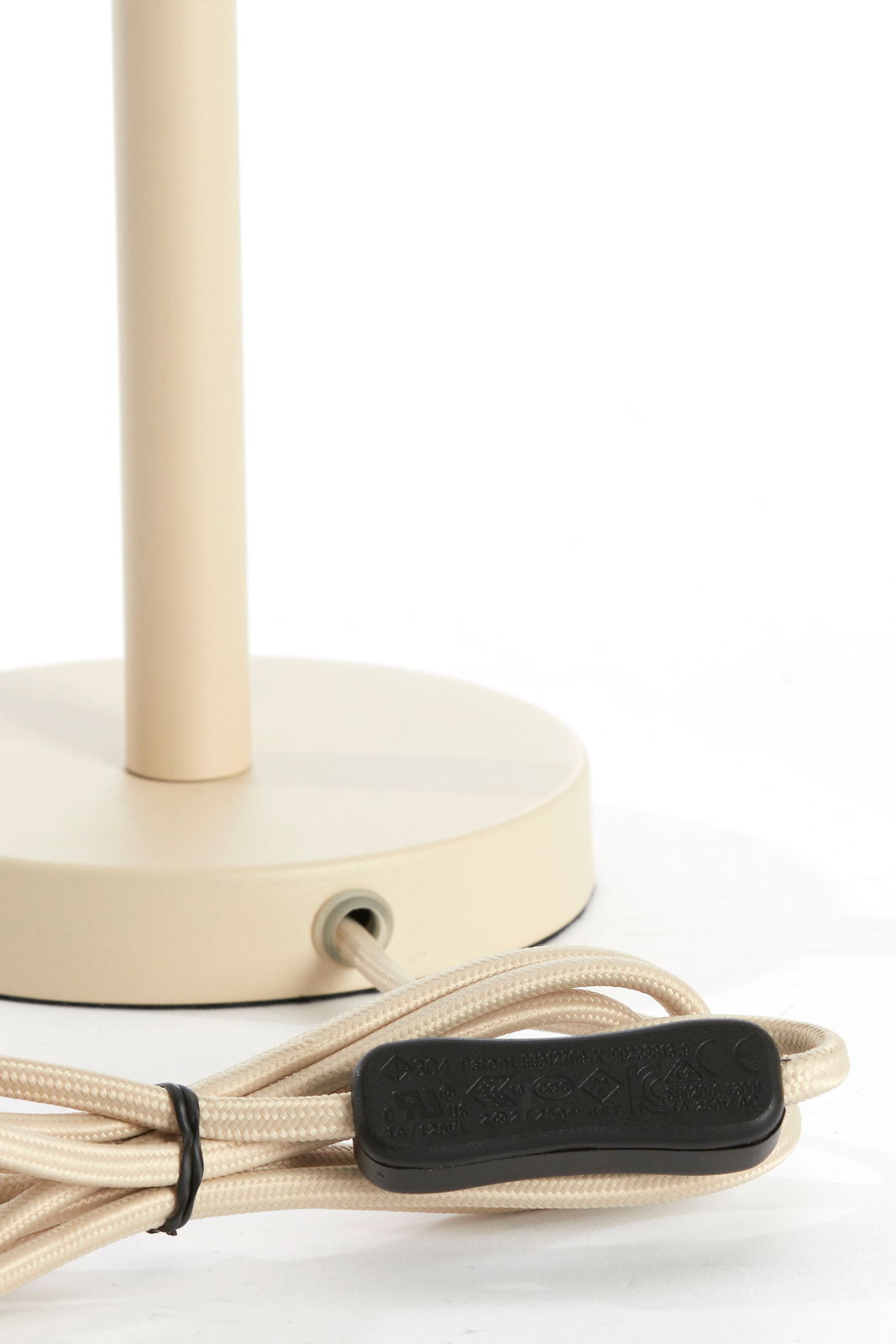 Nahaufnahme eines beigen Lampenfußes mit rundem Sockel und Kabel mit Schalter, seitliche Perspektive.