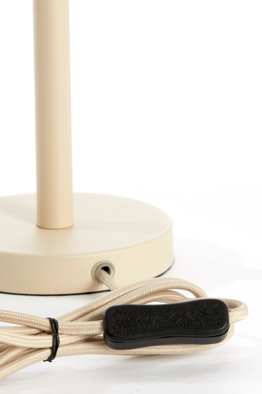 Nahaufnahme eines beigen Lampenfußes mit rundem Sockel und Kabel mit Schalter, seitliche Perspektive.