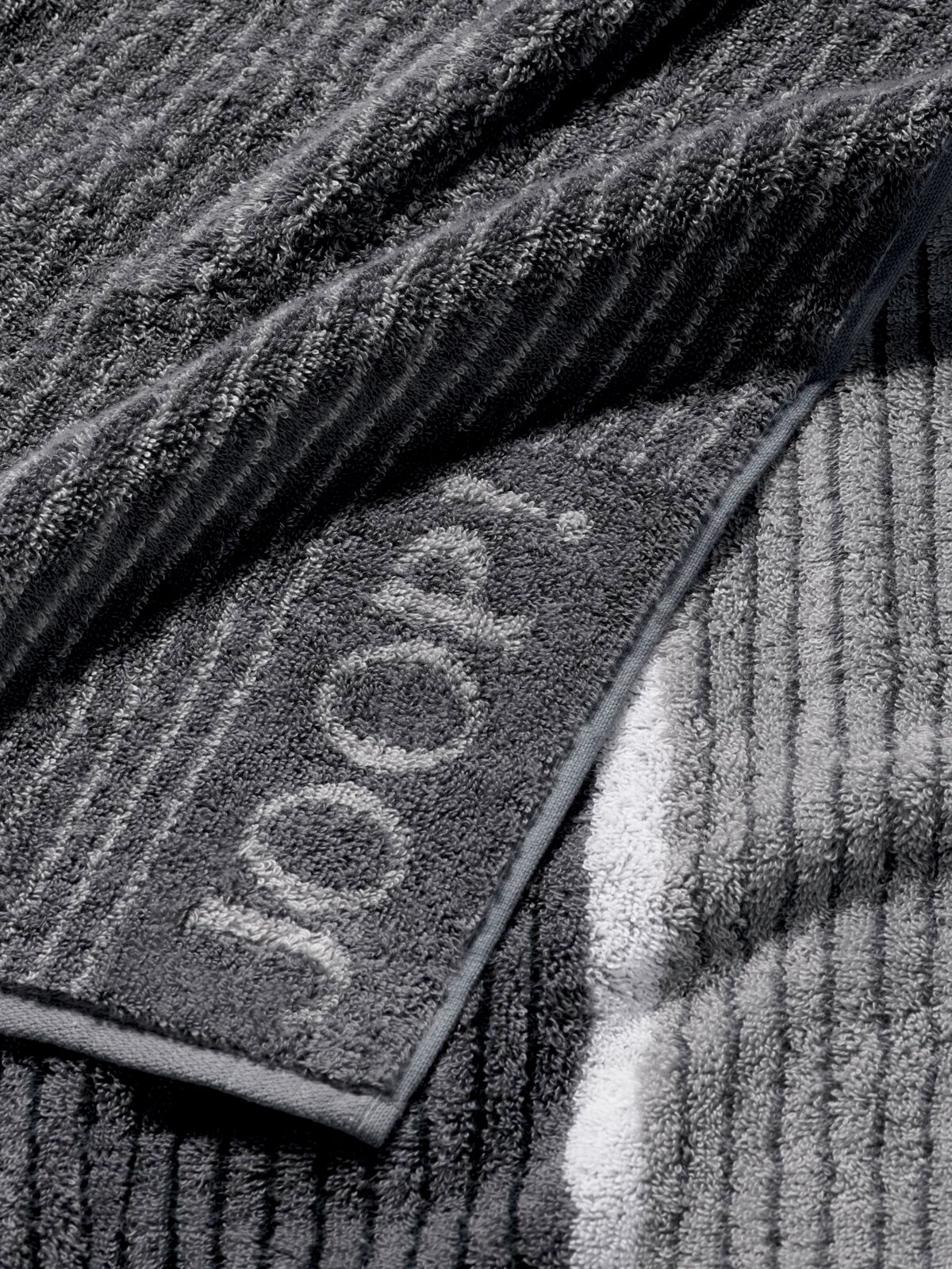 Grijze saunadoek met ingeweven logo, close-up van de textuur en het ontwerp.