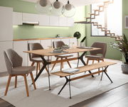 Moderner Essbereich mit einem Esstisch und Sitzbank aus Holz und Metall, umgeben von gepolsterten Stühlen in einem hellen Raum mit grüner Wand und Treppe im Hintergrund. Perspektive: seitliche Ansicht.