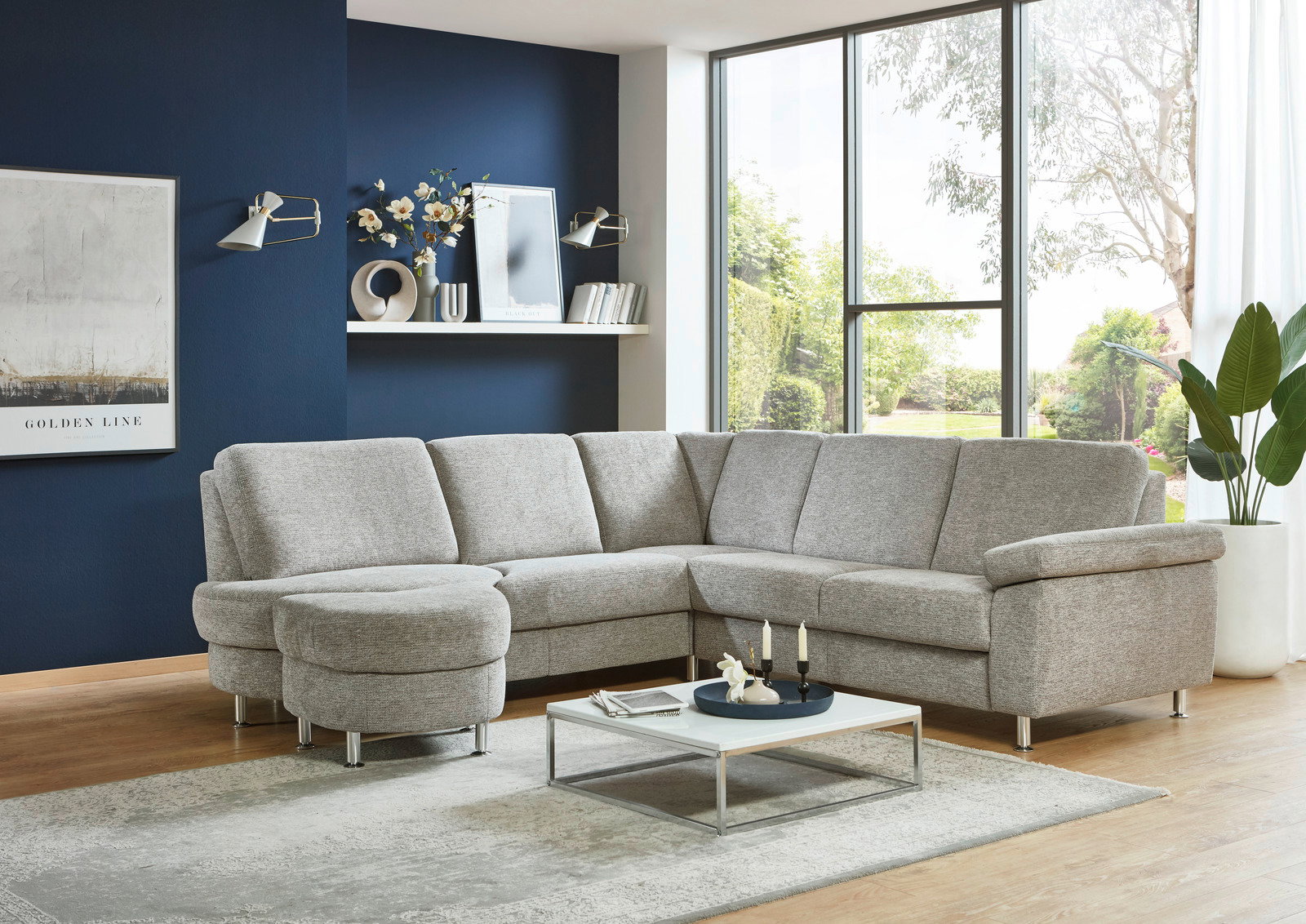 Graue Eckgarnitur in modernem Wohnzimmer mit blauer Wand und großem Fenster, seitliche Perspektive