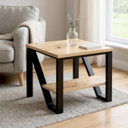 Moderner Beistelltisch mit heller Holzplatte und schwarzem Metallgestell samt Ablage, im Wohnzimmer neben einem grauen Sofa; Perspektive: leicht schräg von vorne auf Tischhöhe.