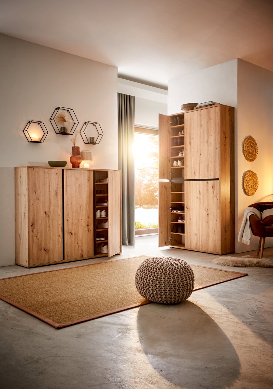 Schuhschrank aus Holz in einem modernen Wohnzimmer, mit geöffneter Tür, die mehrere Regale mit Schuhen zeigt. Perspektive von vorne links.