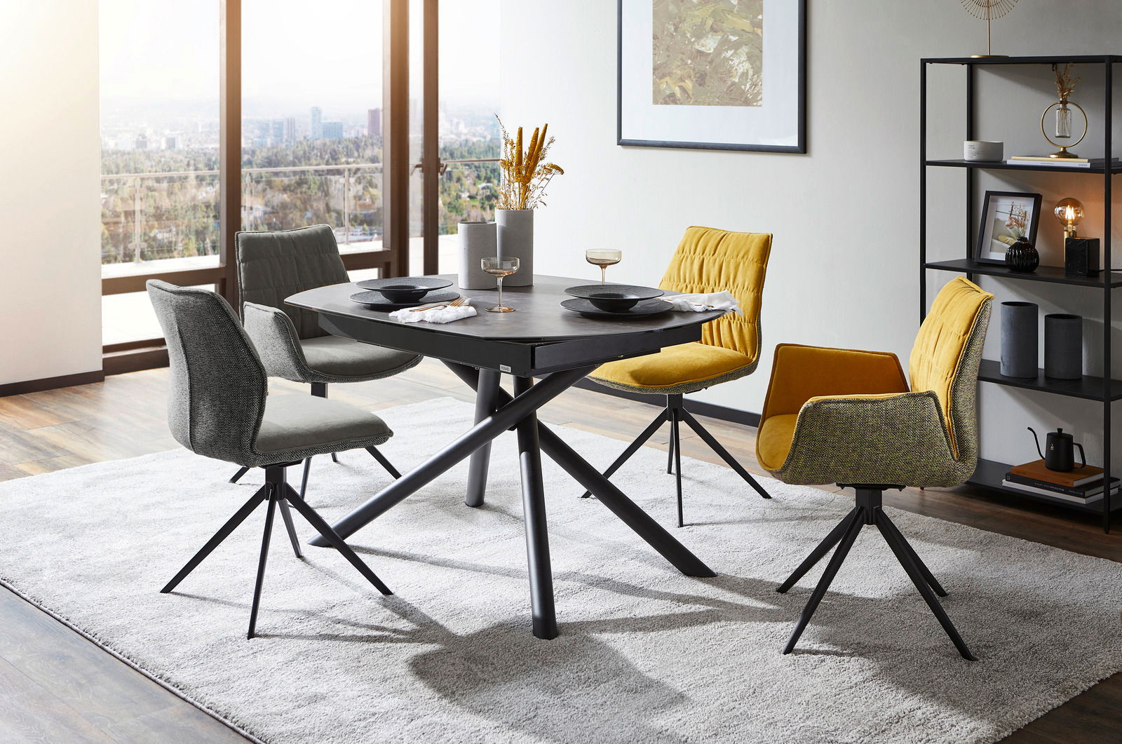 Moderner Esstisch mit schwarzer Tischplatte und gekreuzten Beinen, umgeben von stilvollen Stühlen in einem hellen Raum mit Stadtblick, aus seitlicher Perspektive.