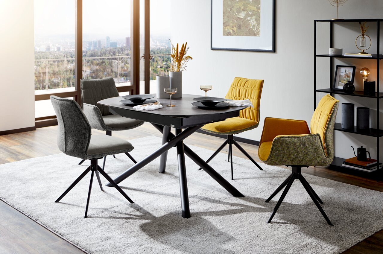 Moderner Esstisch mit schwarzer Tischplatte und gekreuzten Beinen, umgeben von stilvollen Stühlen in einem hellen Raum mit Stadtblick, aus seitlicher Perspektive.