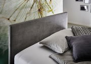 Seitliche Ansicht einer Polsterliege mit grauem Kopfteil und mehreren Kissen in einem modernen Schlafzimmer.