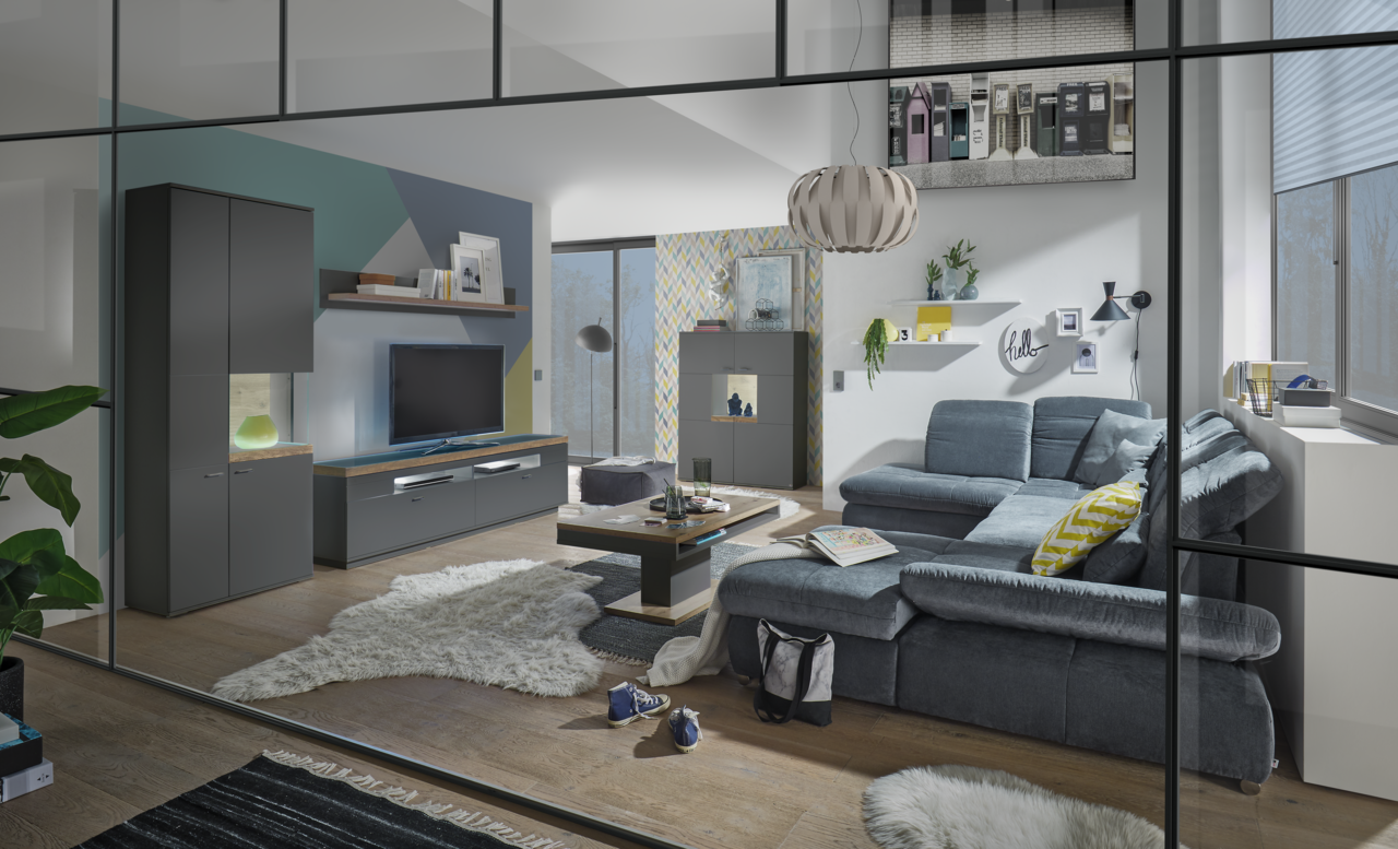Set one by Musterring Vitrine Glasausschnitt rechts SET ONE LANCASTER Moderne Wohnzimmermöbel in einem stilvollen Raum mit grauem Sofa, Couchtisch und TV-Lowboard, Perspektive von vorne.