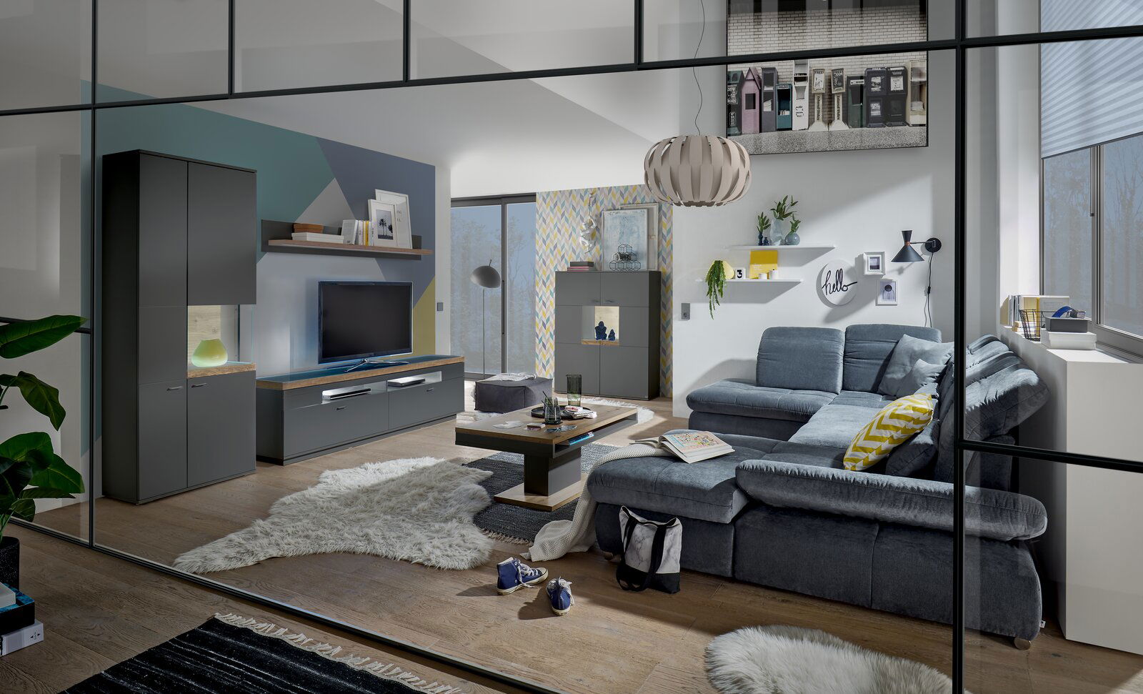 Set one by Musterring Vitrine Glasausschnitt rechts SET ONE LANCASTER Moderne Wohnzimmermöbel in einem stilvollen Raum mit grauem Sofa, Couchtisch und TV-Lowboard, Perspektive von vorne.