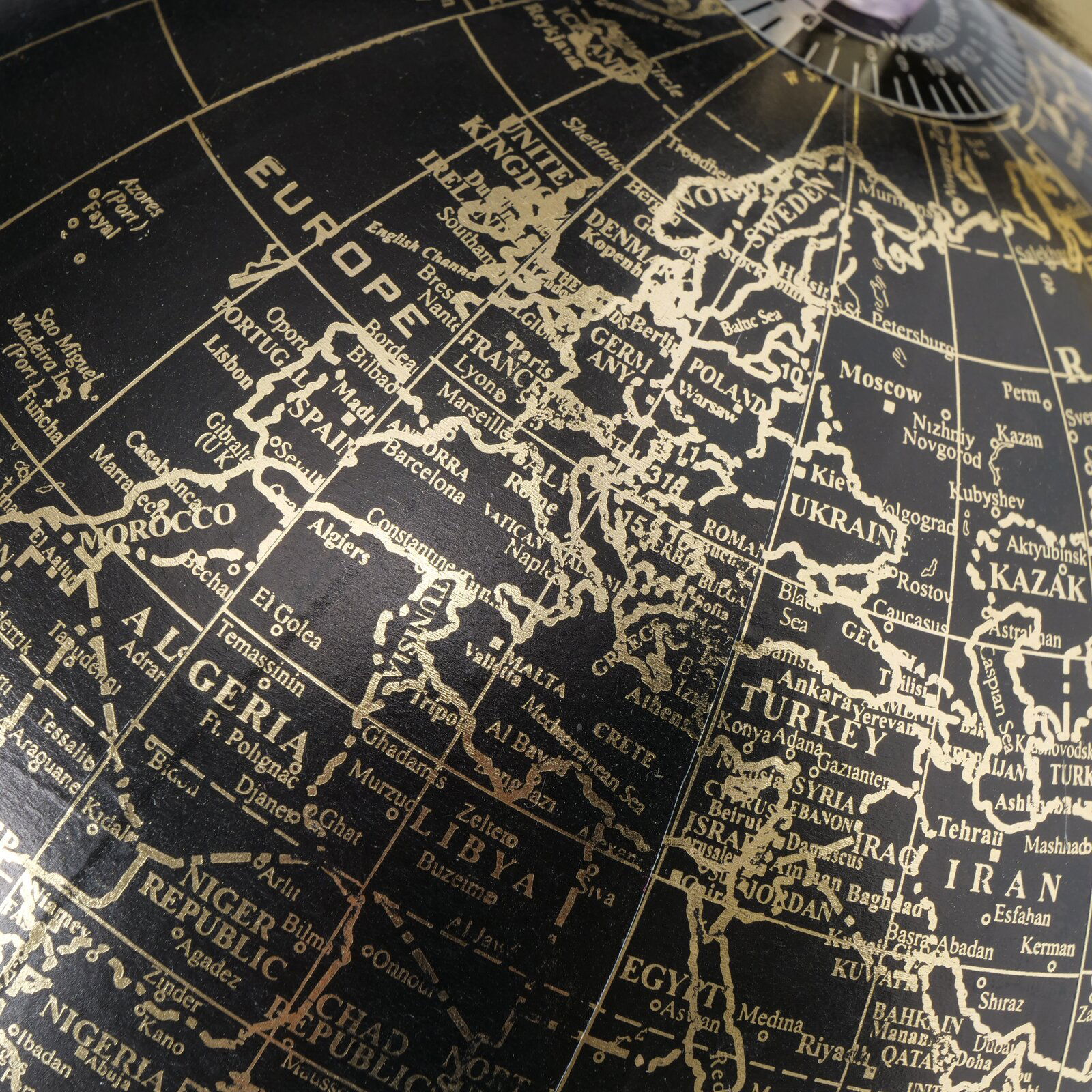 Nahaufnahme eines dekorativen Globus mit goldenen Ländernamen auf schwarzem Hintergrund, Perspektive von oben auf Europa und Nordafrika.