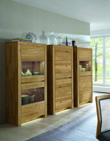 Holzvitrine mit Glaseinsätzen, links im Bild, in einem modernen Wohnzimmer mit Tageslicht.