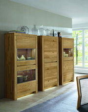 Holzvitrine mit Glaseinsätzen, links im Bild, in einem modernen Wohnzimmer mit Tageslicht.