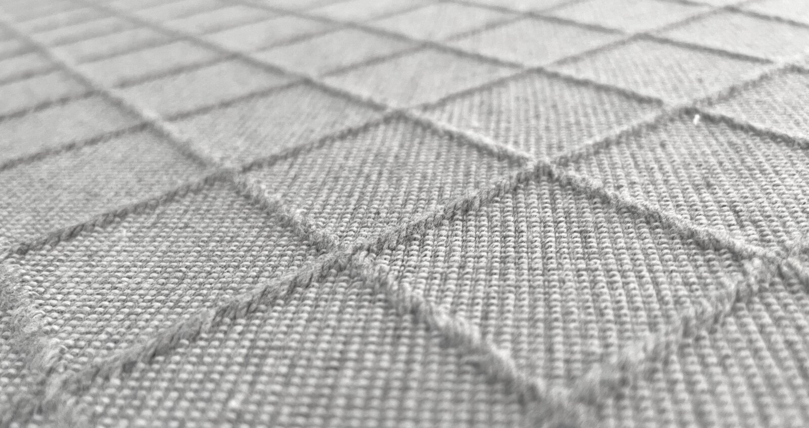 Nahaufnahme einer texturierten Stoffoberfläche mit quadratischem Muster, perspektivisch von der Seite aufgenommen.