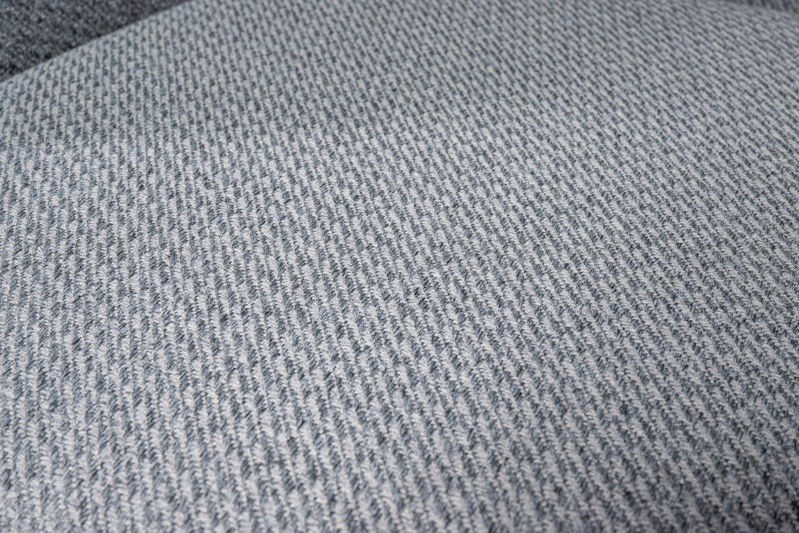 Nahaufnahme eines grauen Stoffbezugs mit feiner Webstruktur, perspektivisch von oben fotografiert.