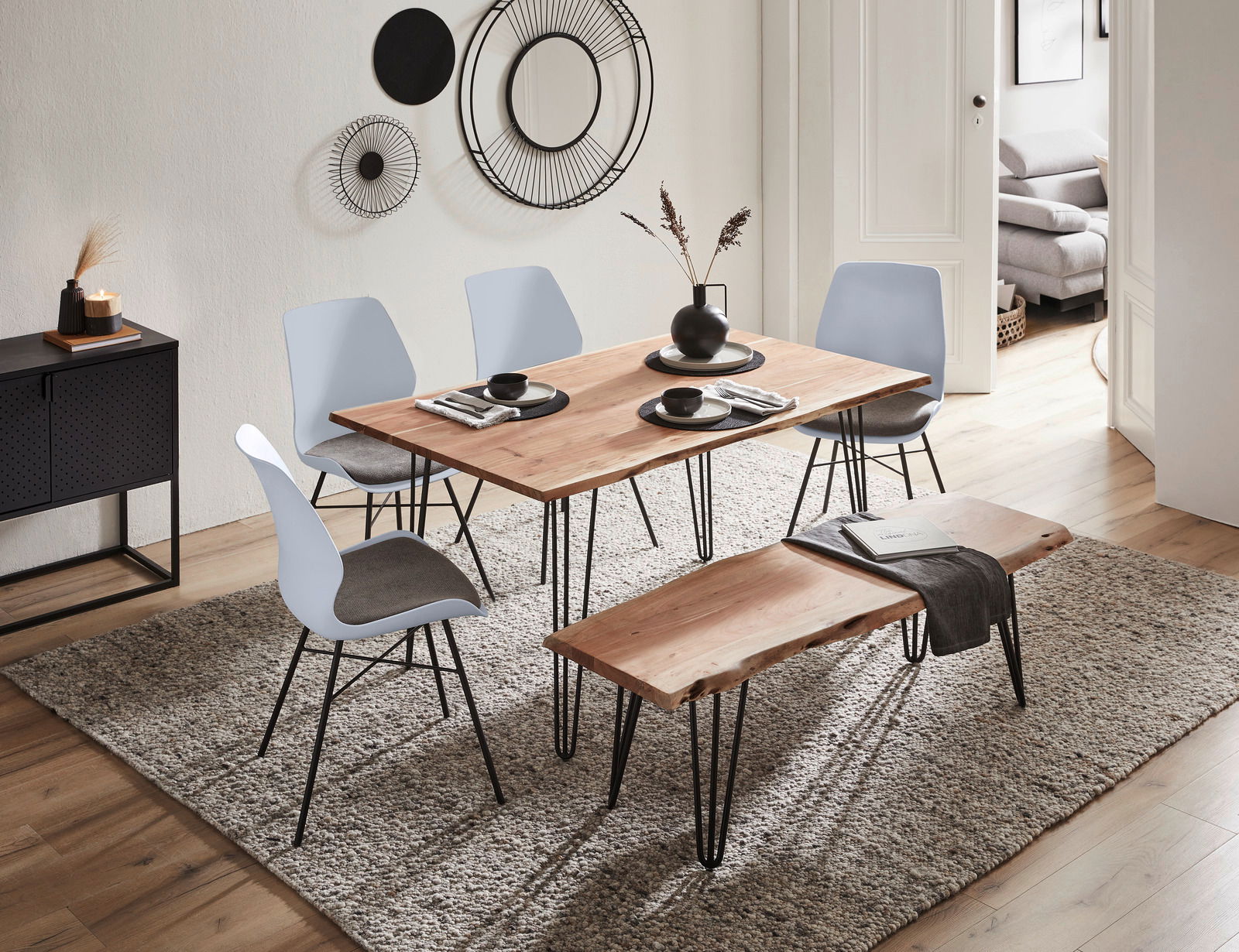Moderner Essbereich mit hellem Holztisch, umgeben von vier hellblauen Stühlen mit grauen Sitzflächen, aus seitlicher Perspektive fotografiert.