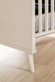 Detailaufnahme eines weißen Babybetts/Kinderbetts mit Gitterstäben und schrägem Holzfuß, seitliche Nahperspektive von unten