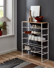 Modernes Schuhregal mit weißem Metallgestell und Holzablage, seitliche Perspektive im Flur, mit mehreren Paar Schuhen und Deko auf der Oberseite.