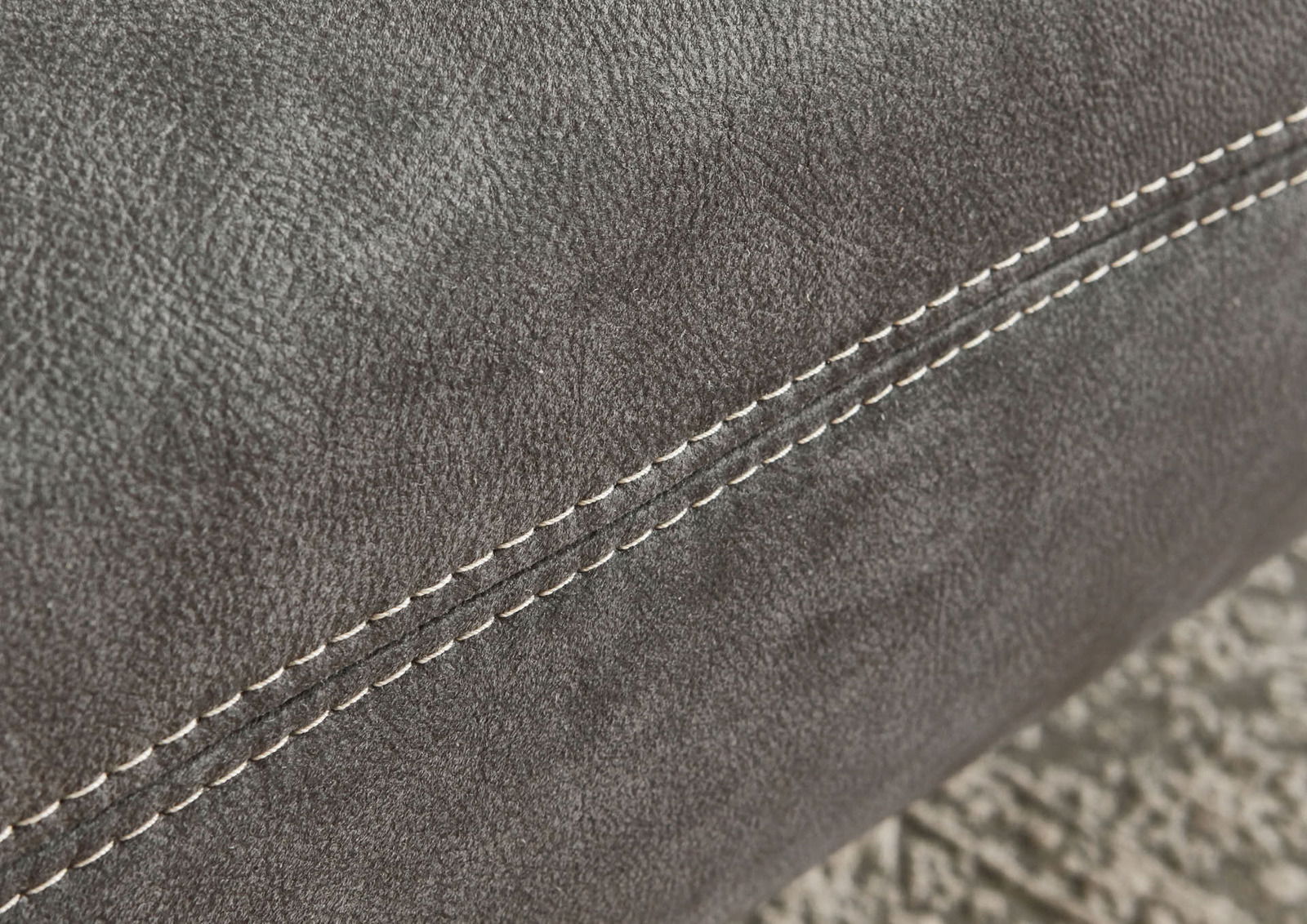 Nahaufnahme einer grauen Stoffoberfläche mit sichtbarer Naht, perspektivisch von der Seite aufgenommen.