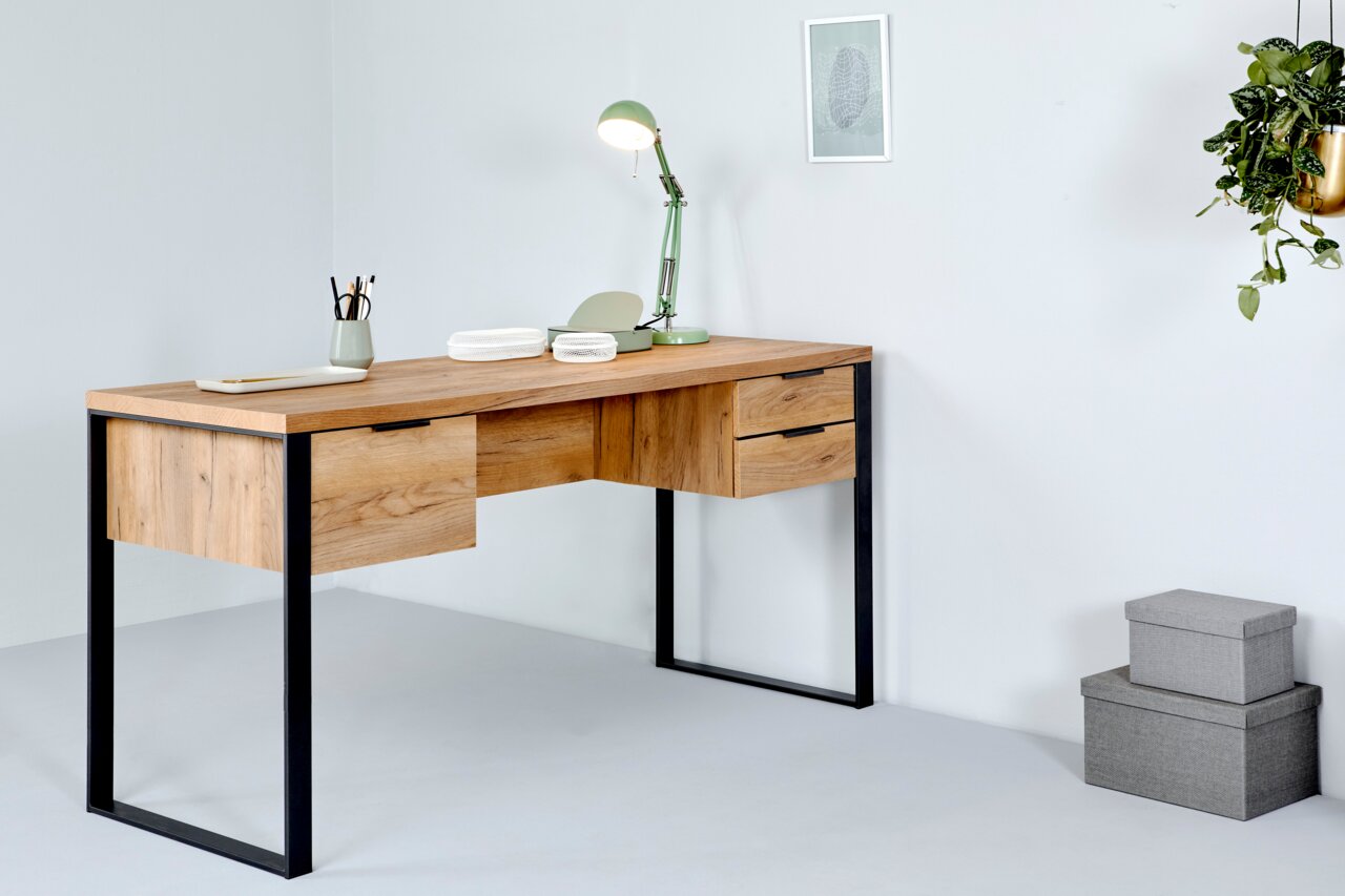 Moderner Schreibtisch aus Holz mit schwarzen Metallbeinen, seitliche Perspektive, dekoriert mit einer grünen Lampe und Schreibutensilien.