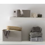 Zwei beige Aufbewahrungskörbe auf weißen Regalen, einer mit einem Gürtel und der andere mit Kleidung und Tüchern, seitliche Perspektive.