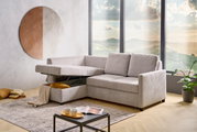 Grijze functionele hoekbank met opbergruimte, gezien vanaf de zijkant, in een moderne woonkamer met een groot raam en een decoratieve spiegel.