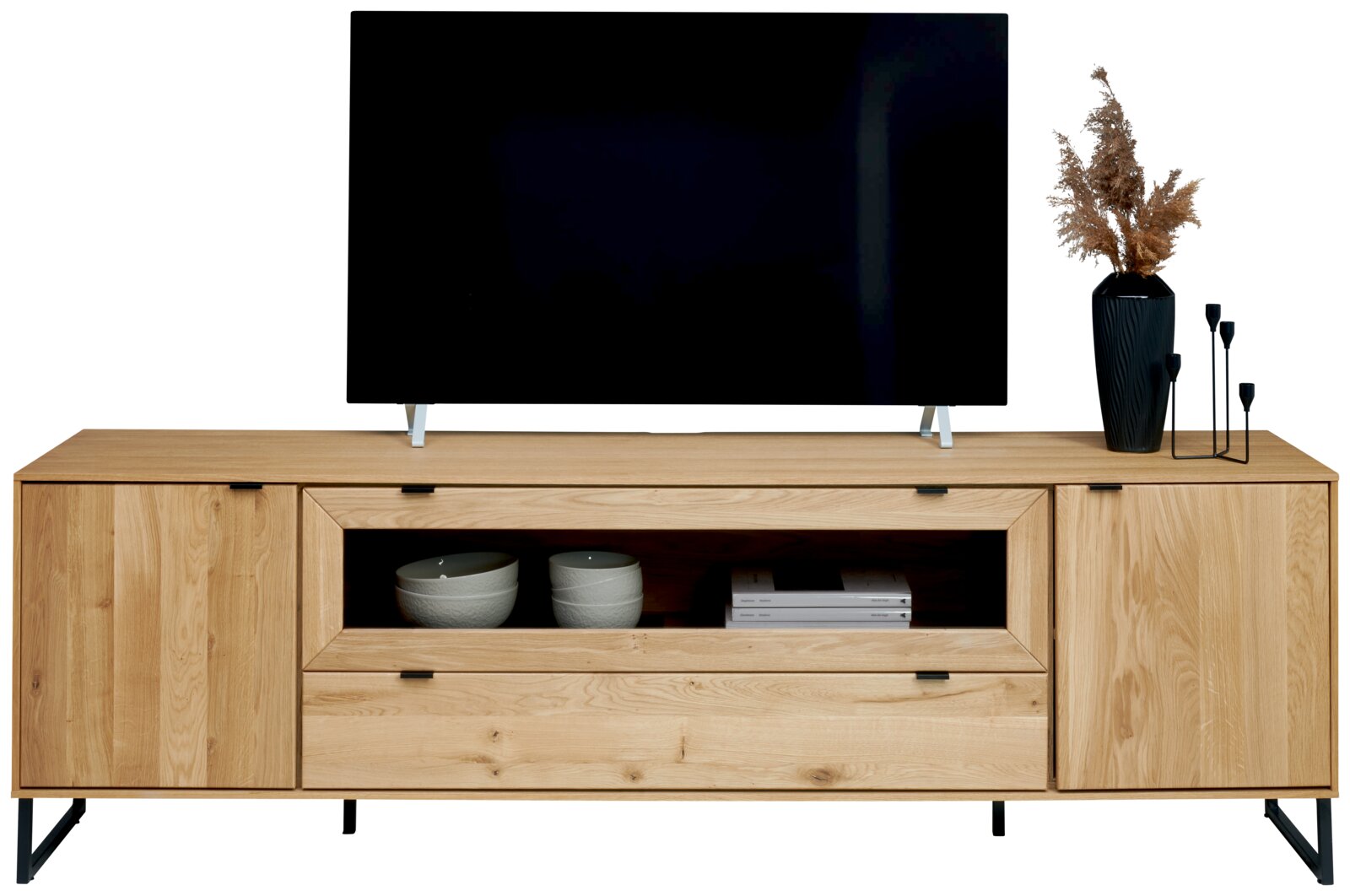 Houten tv-meubel in licht eiken met twee kastdeuren, open vak en lade op zwart metalen poten, gefotografeerd van voren op ooghoogte.