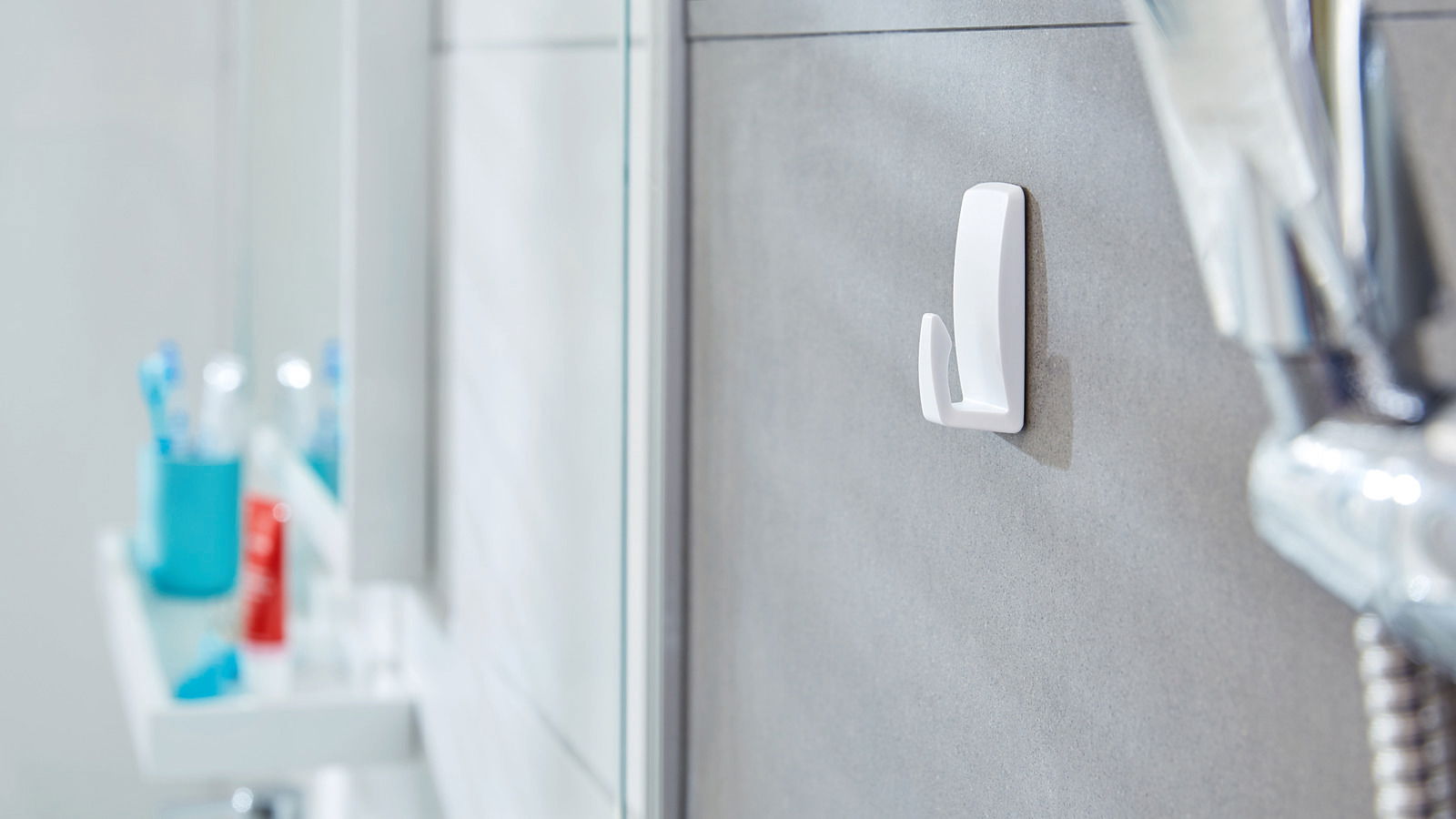 Wandhaken im Badezimmer, seitliche Perspektive, befestigt an einer grauen Fliese, mit verschwommenem Hintergrund von Badezimmerutensilien.
