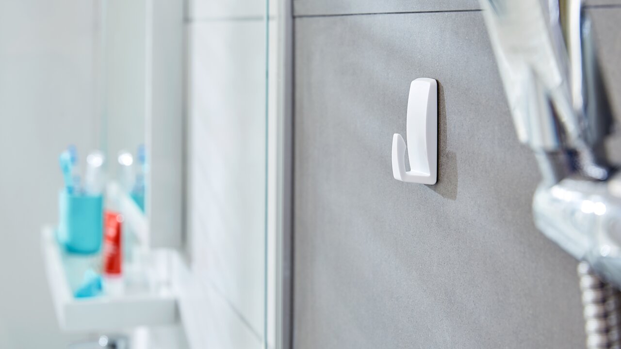 Wandhaken im Badezimmer, seitliche Perspektive, befestigt an einer grauen Fliese, mit verschwommenem Hintergrund von Badezimmerutensilien.