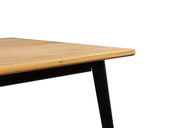 Nahaufnahme eines Esstisches mit Holzplatte und schwarzen Metallbeinen, seitliche Perspektive.